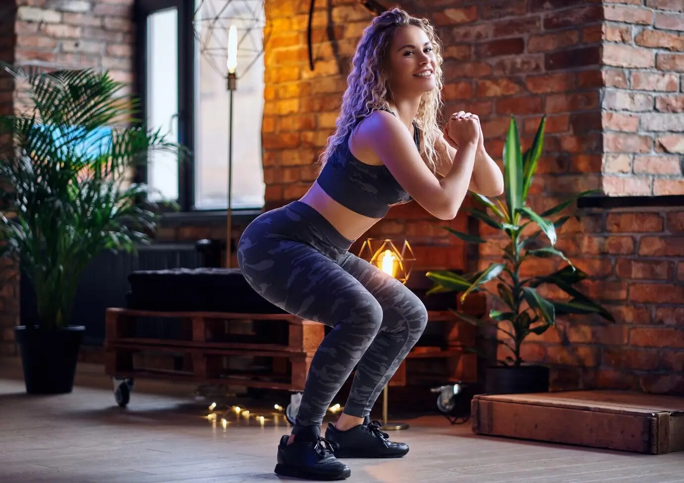 Beintraining für eine Frau. Eine blonde, sportliche Frau macht Kniebeugen in einem Raum im Loftstil.